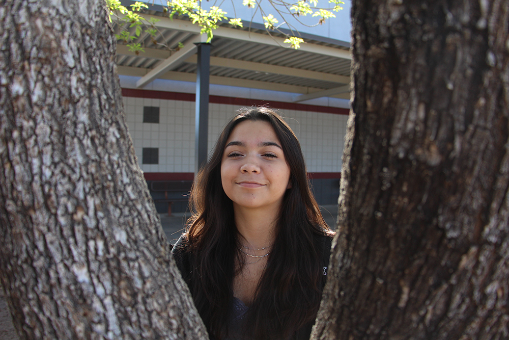 Alexia smiling between the branches of a tree.