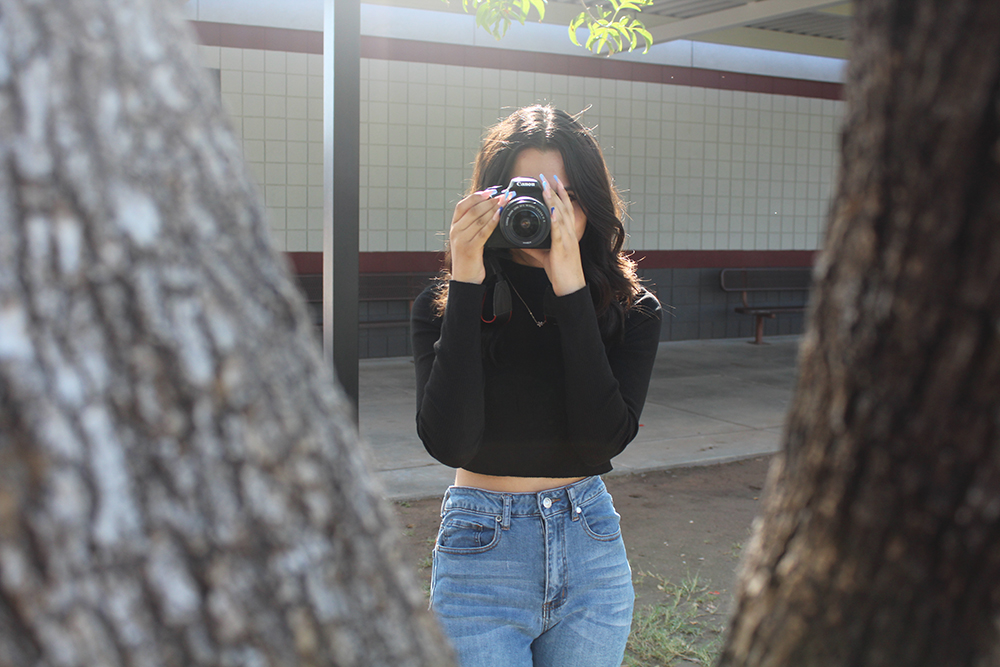 Alexia holding a camera over her face in the courtyard.